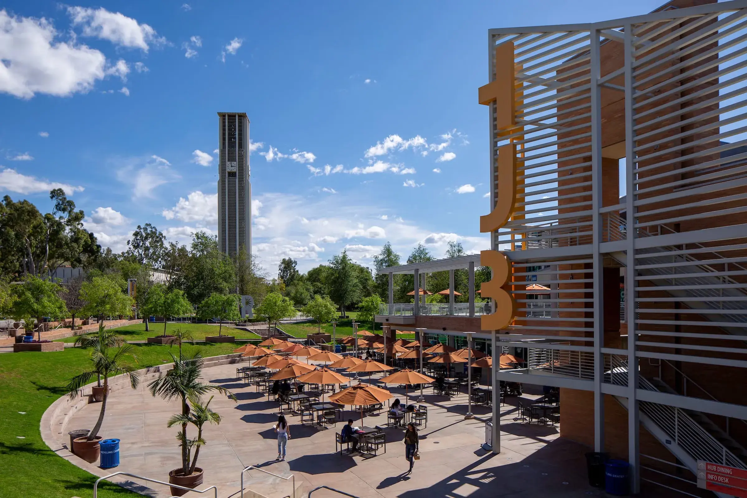 The Highlander Union Building plaza, orange umbrellas over outdoor tables with the bell tower behind