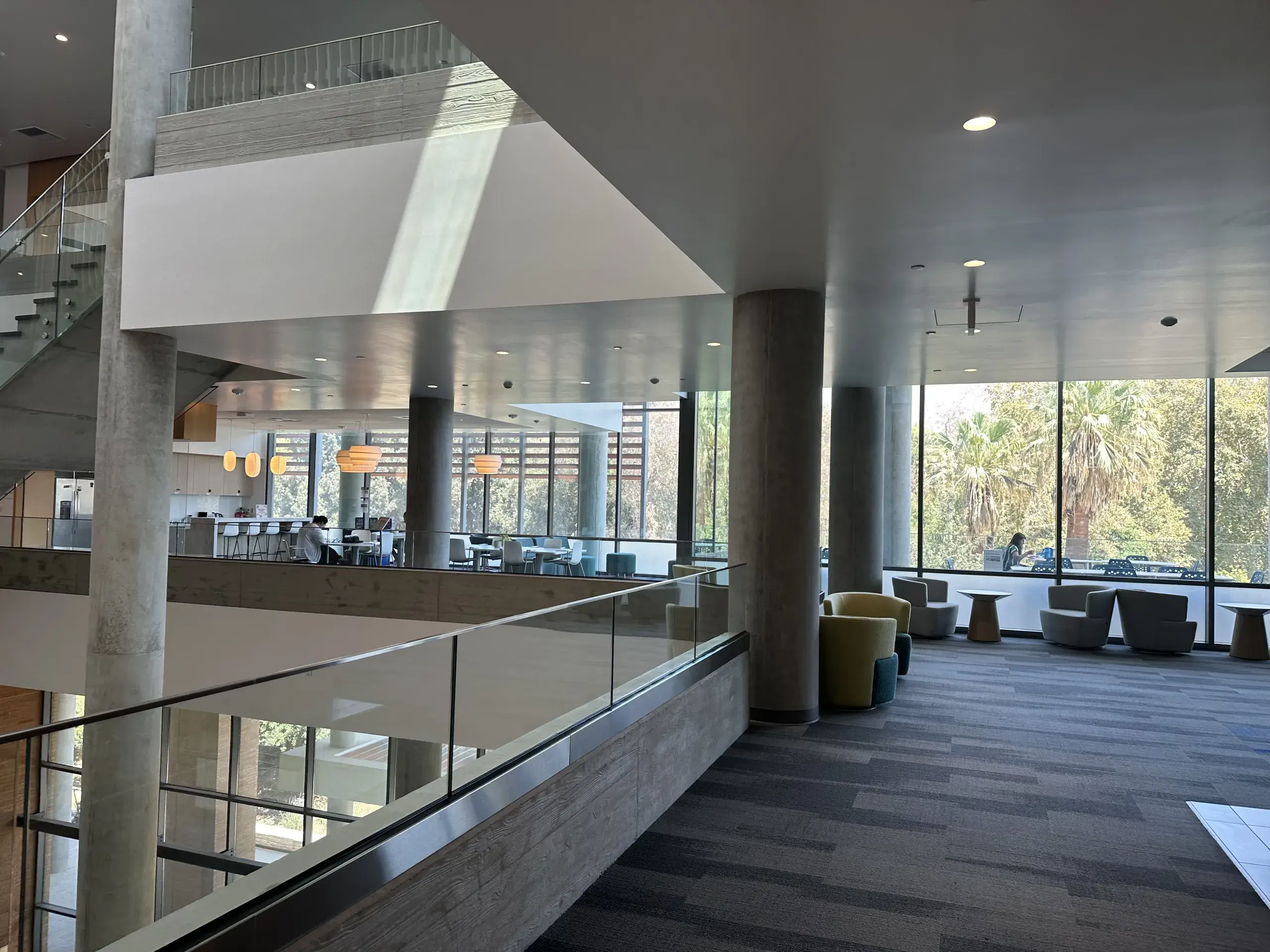 An open common space on an upper floor, seating and tables beside floor-to-ceiling glass