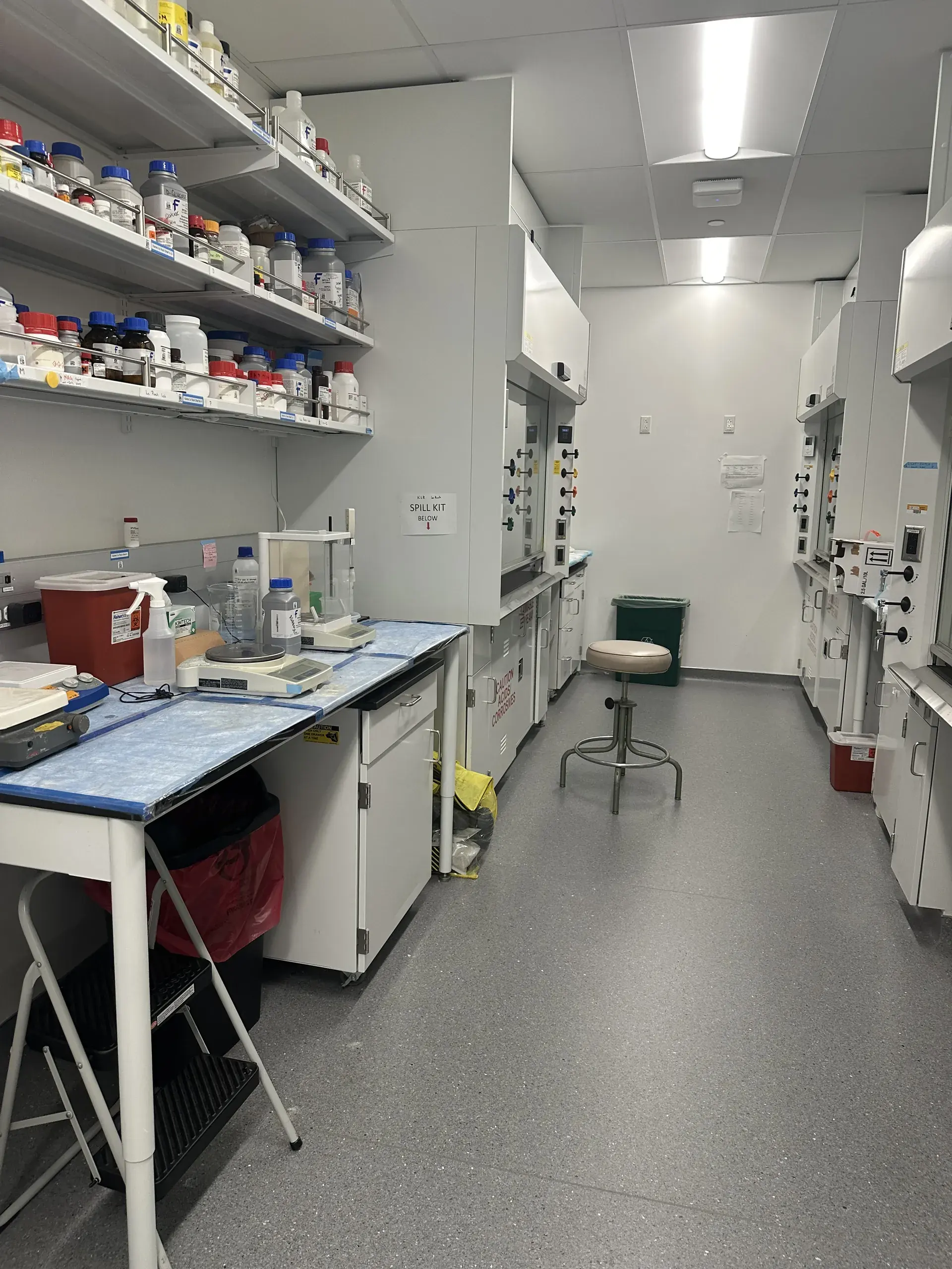 A narrow prep room, bench and stool between shelved supplies